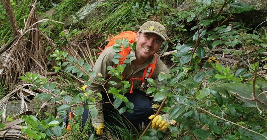 A park ranger in the bush, smiling into the camera.